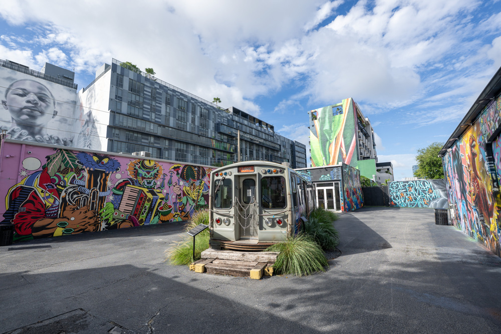 A retired trolley car sits in a courtyard surrounded by large murals